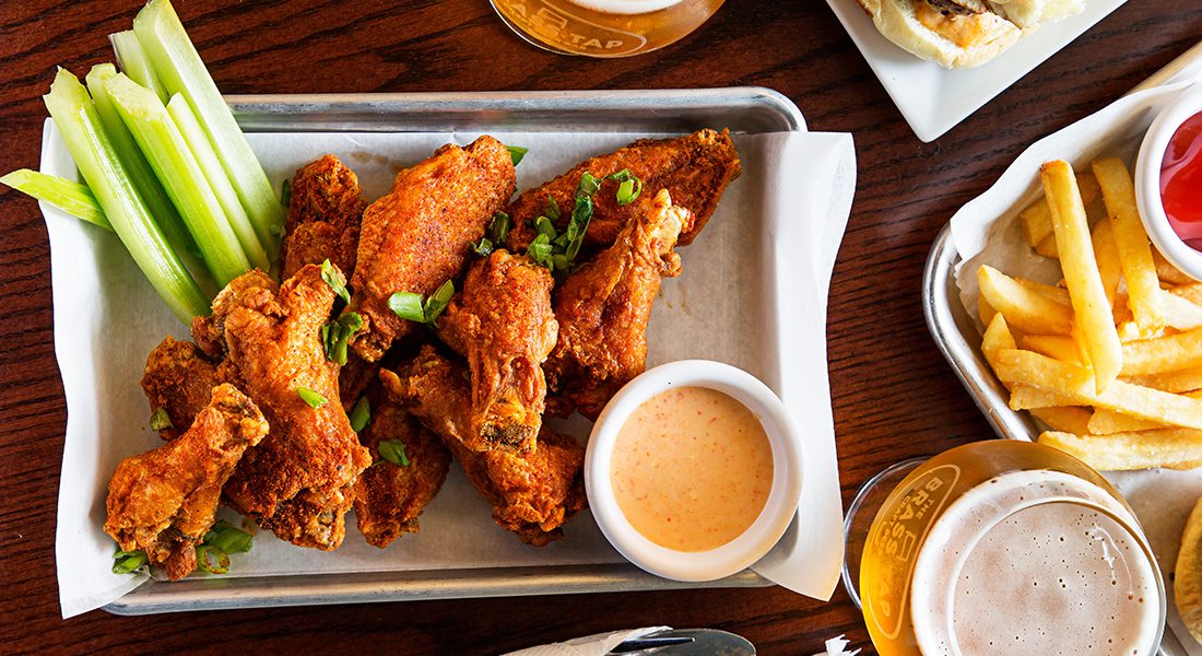 A platter of wings with celery and dipping sauce, a tray of fries, and glasses of beer