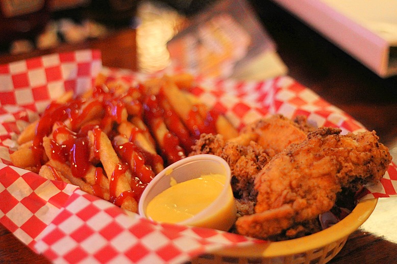 A basket of chicken tenders and fries, with ketchup and mustard