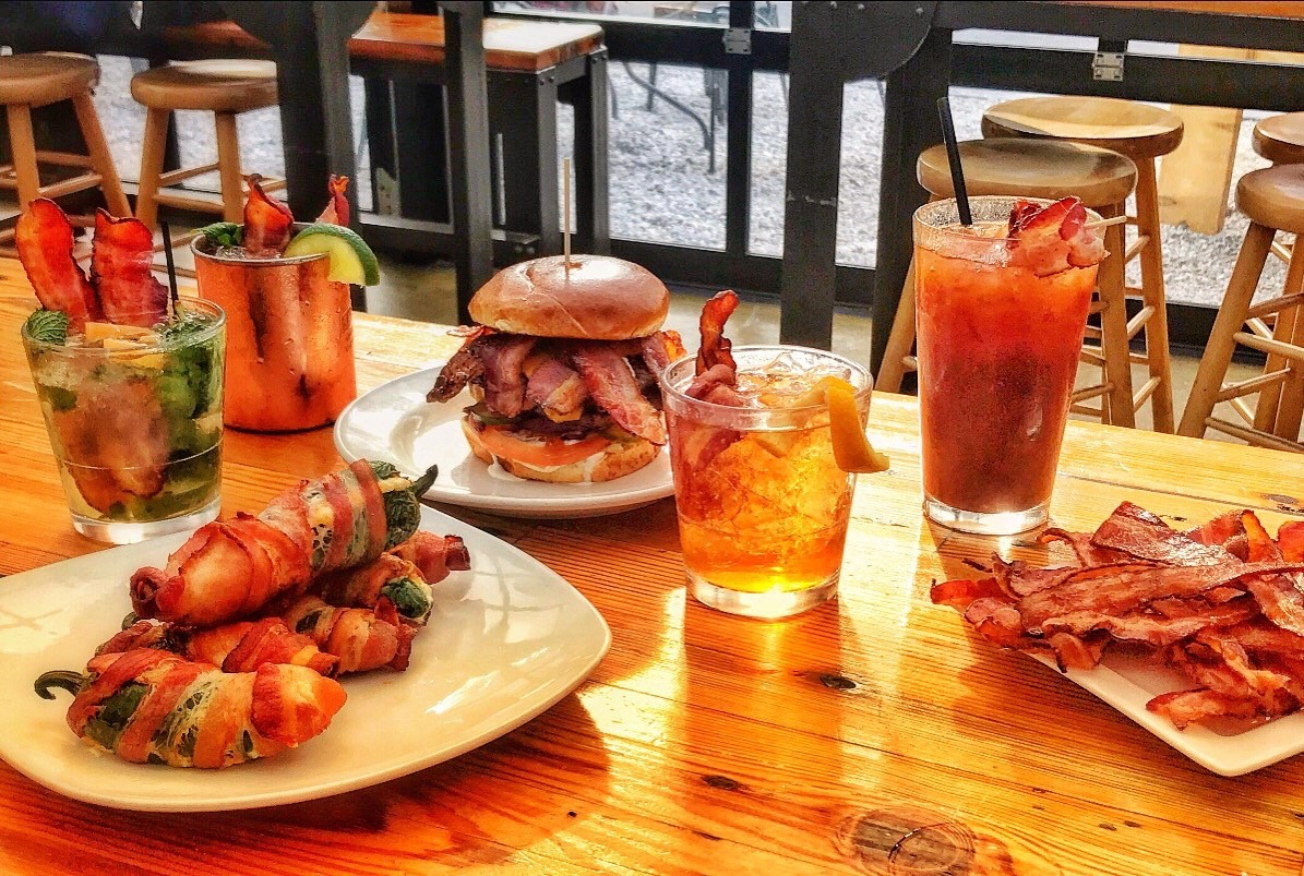 three plates of food, including jalapeno poppers, a burger, and bacon, and four drinks on a table