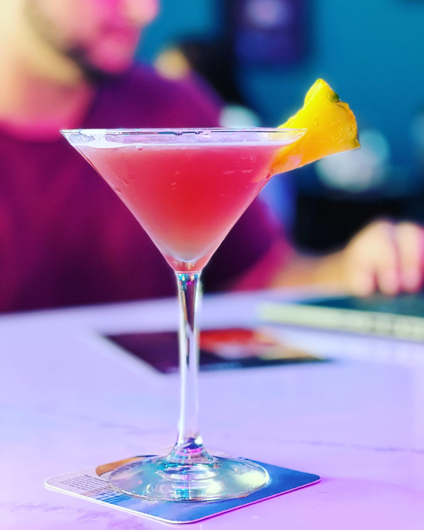 pink mixed drink with a pineapple chunk on the bar top