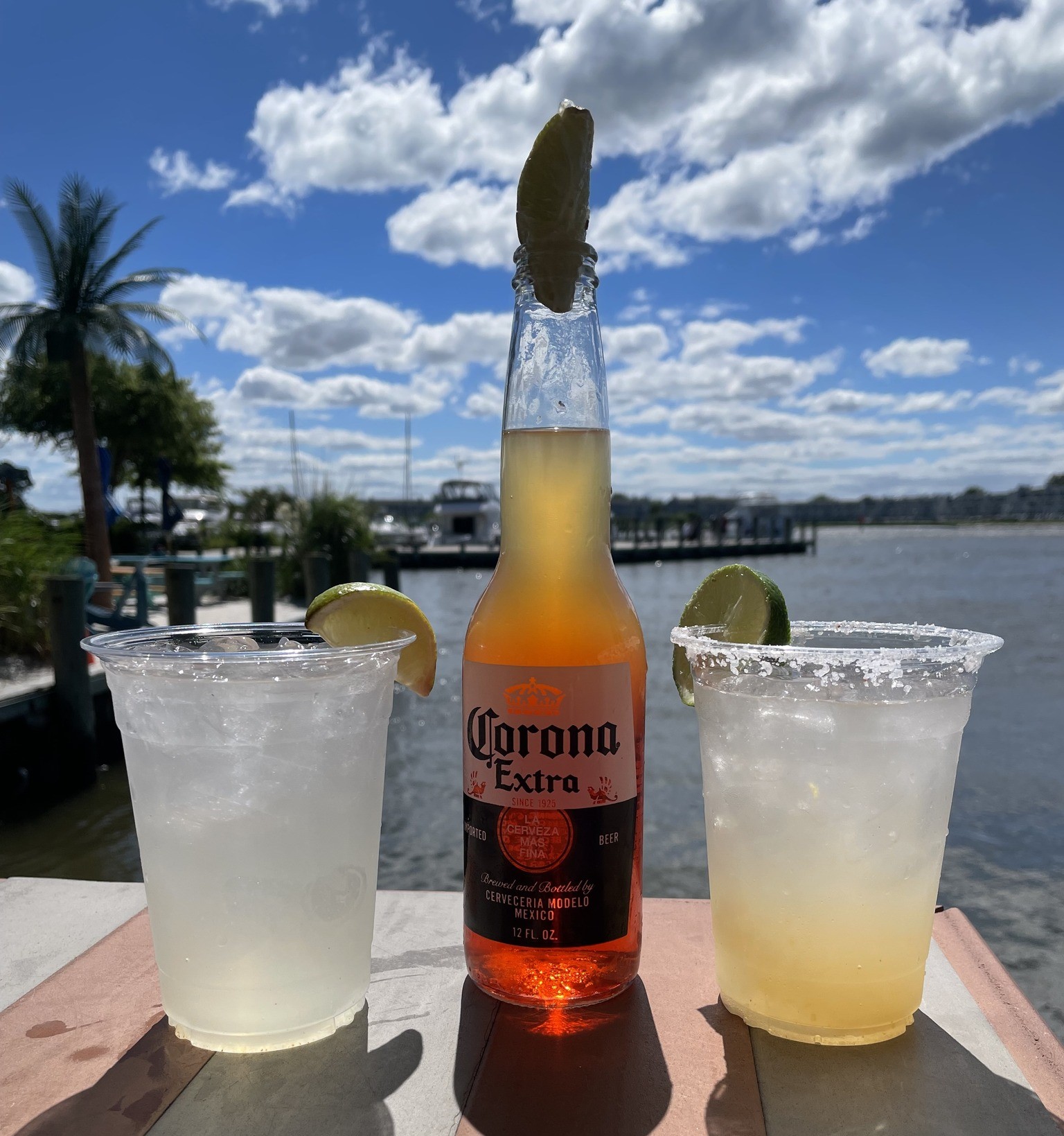 a bottle of beer and two drink cups on a dockside table 