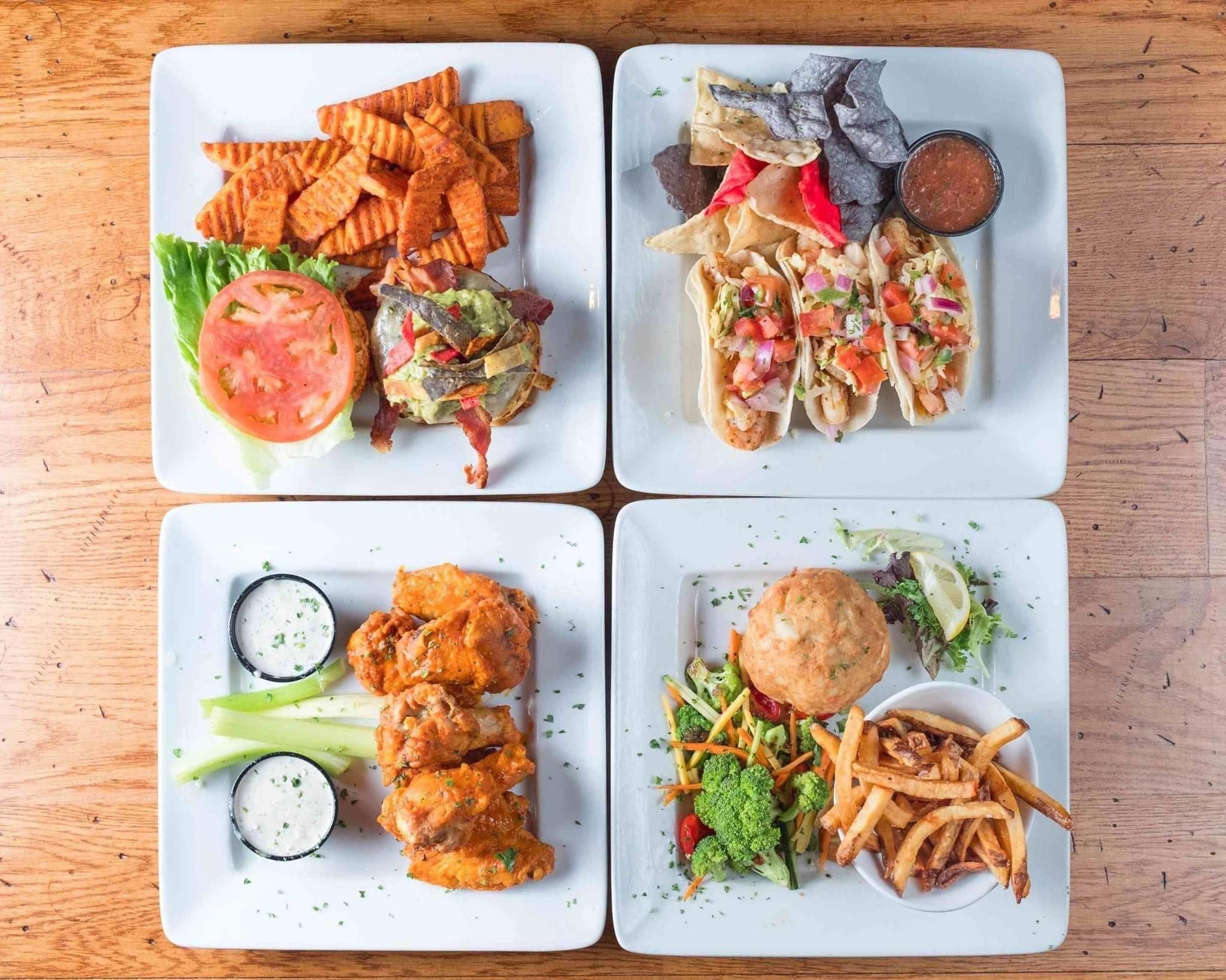 four plates of food on a table, including wings and tacos