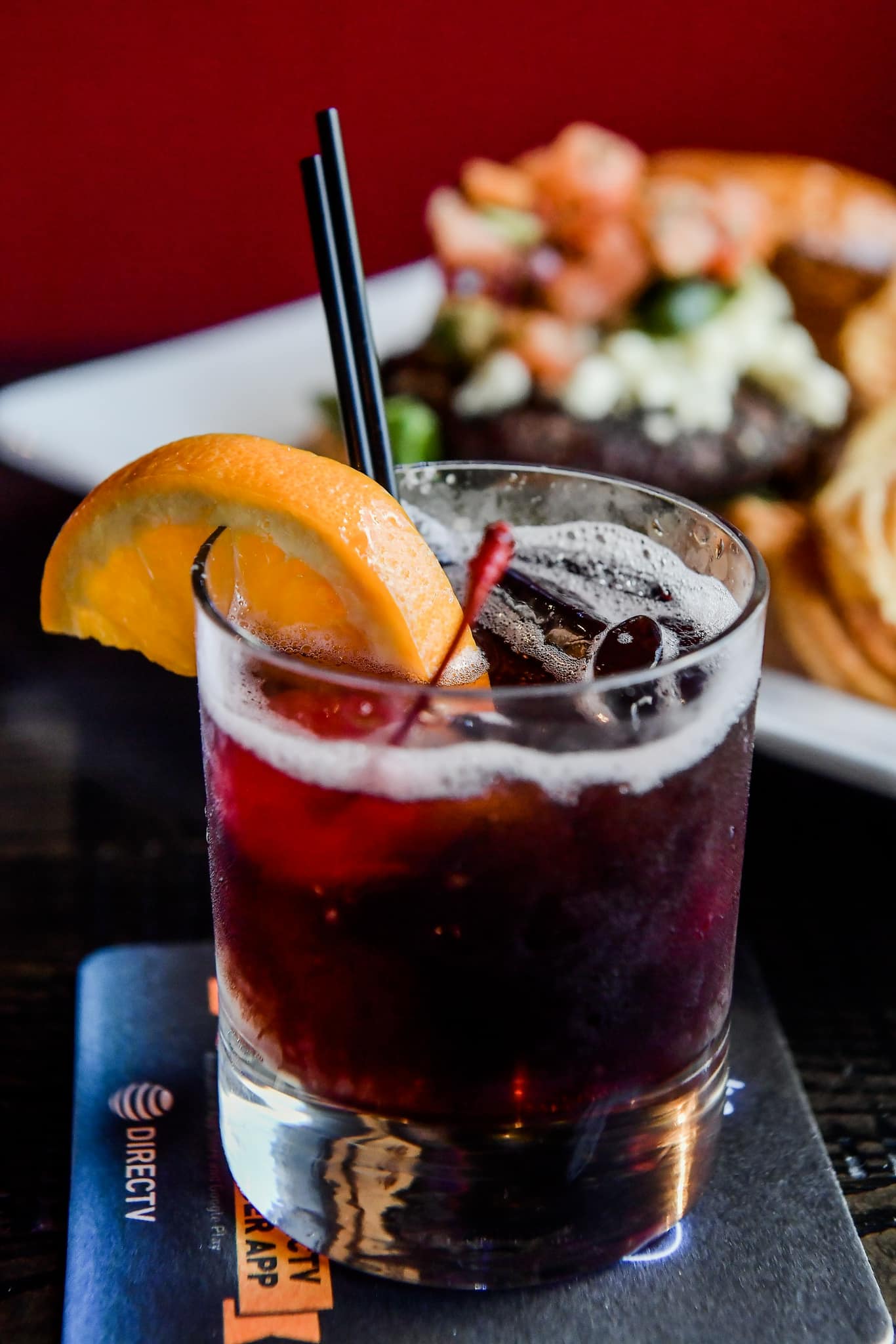 a dark red cocktail with a cherry and an orange slice