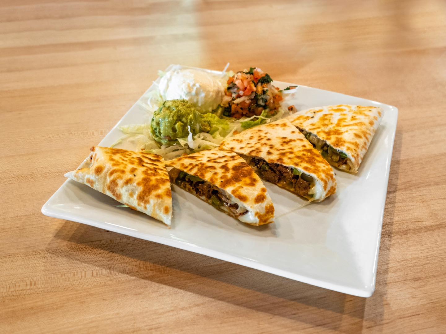 a quesadilla with guacamole, sour cream, and pico de gallo
