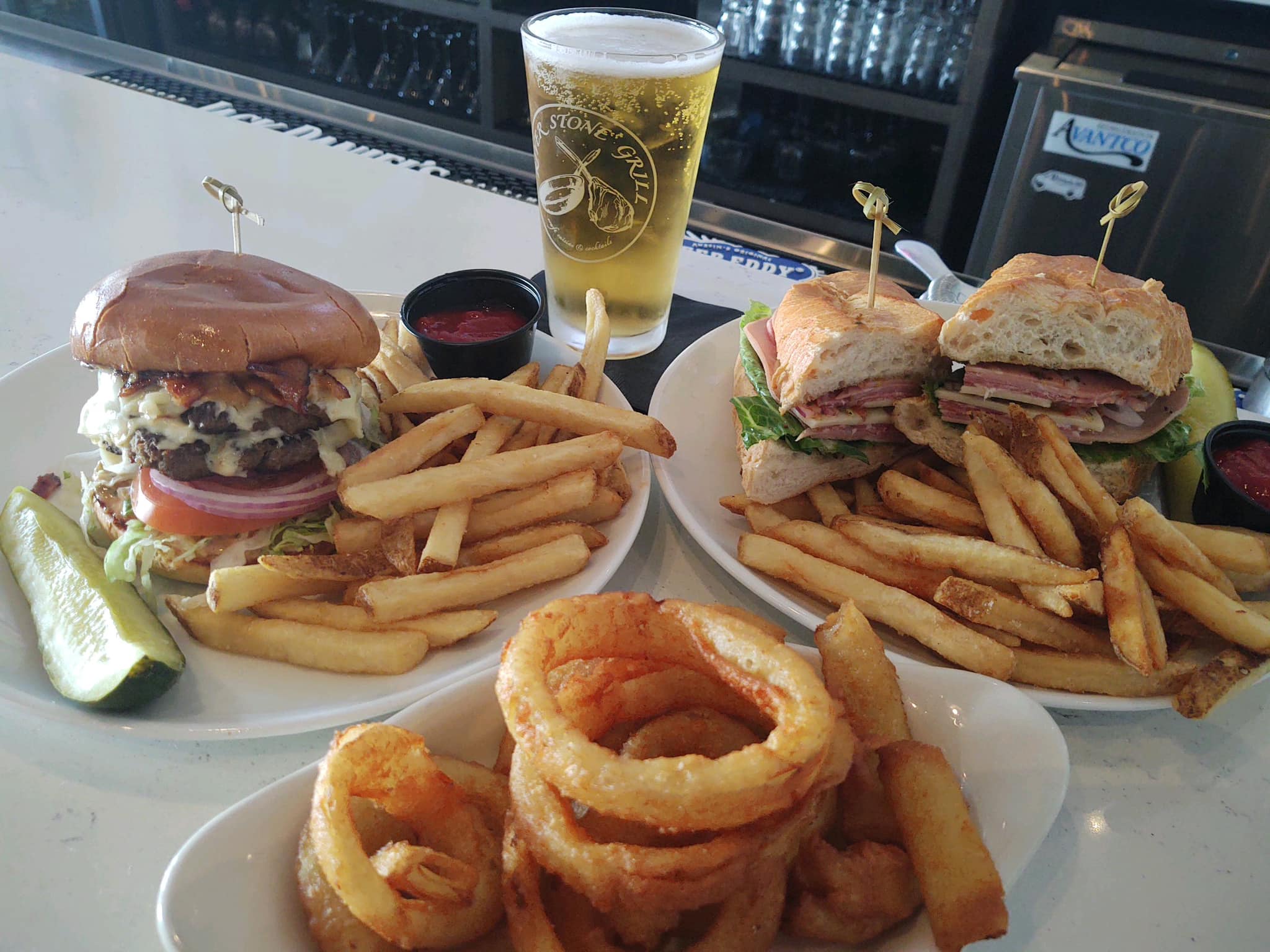 a double smash burger with fries, a Tony D italian sub with fries, onion rings, and a glass of beer