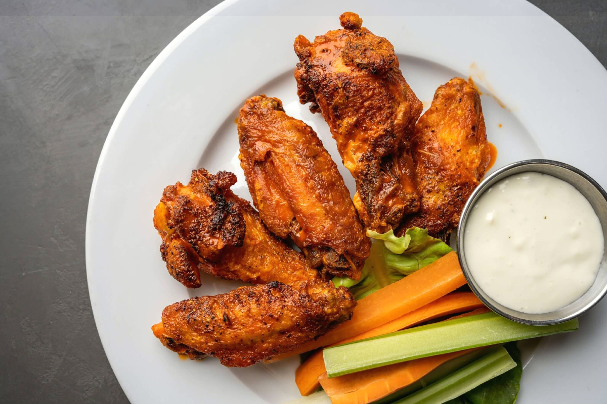 a plate of wings with celery, carrots, and dip