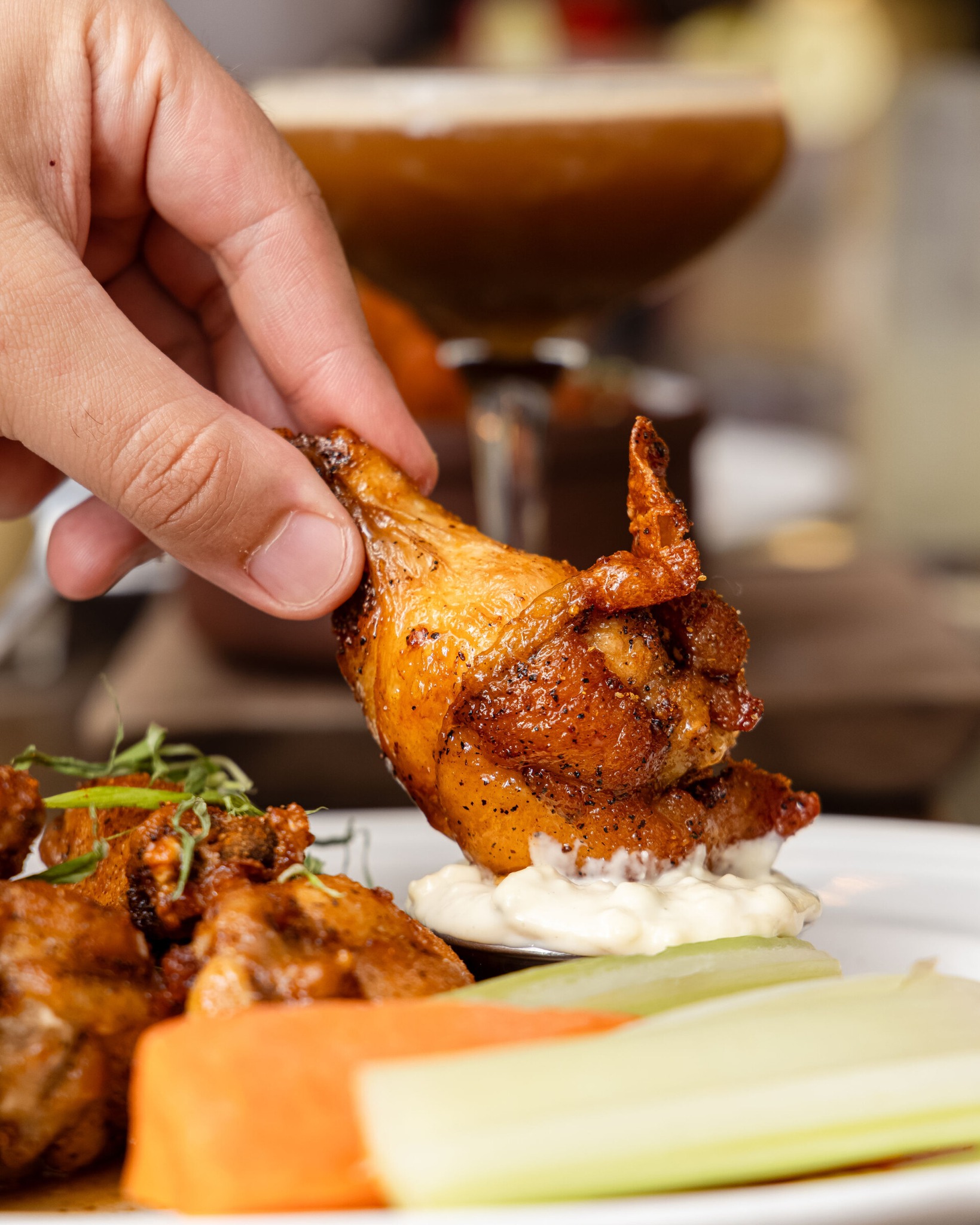a hand dipping a wing into sauce