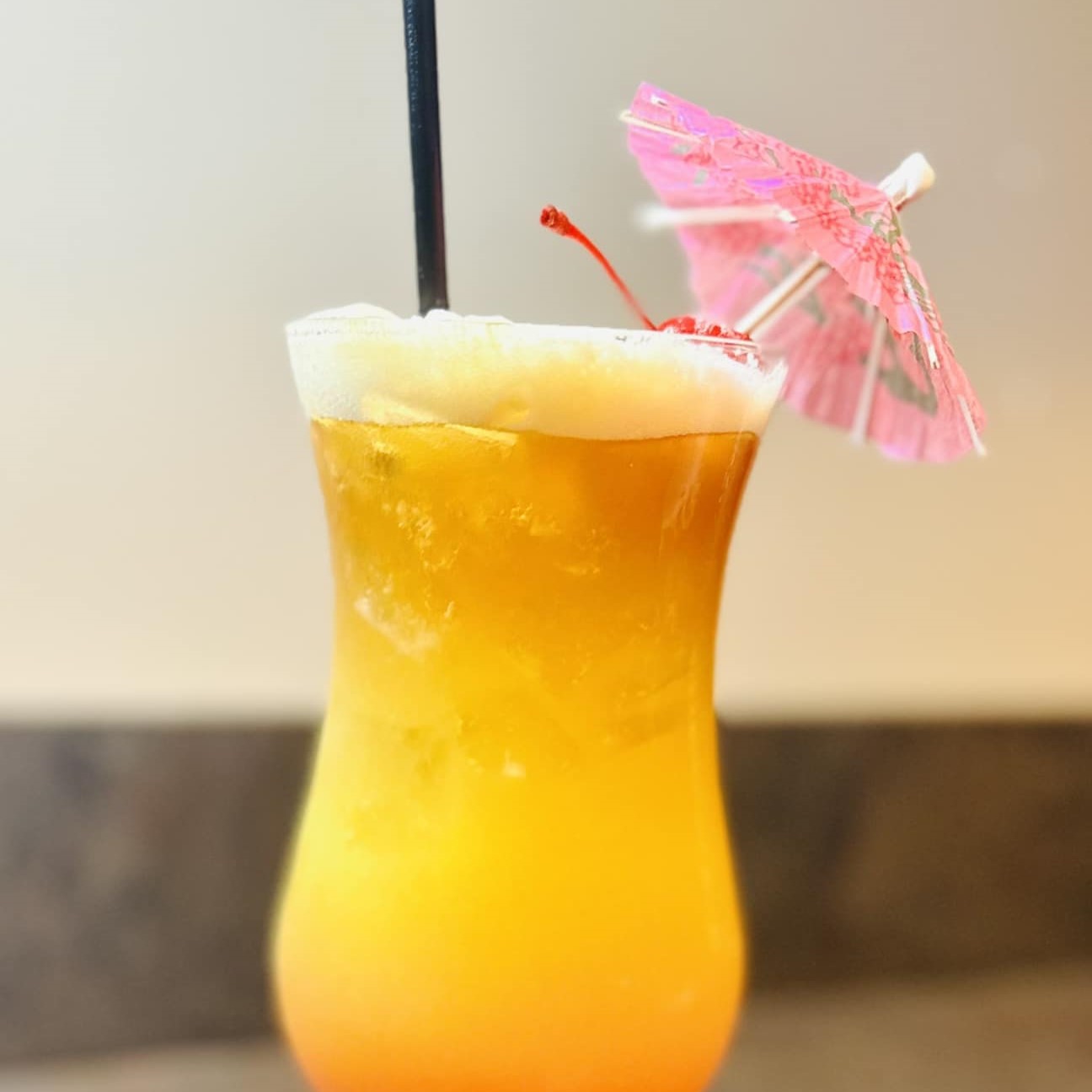 a hurricane cocktail with a pink umbrella and a straw