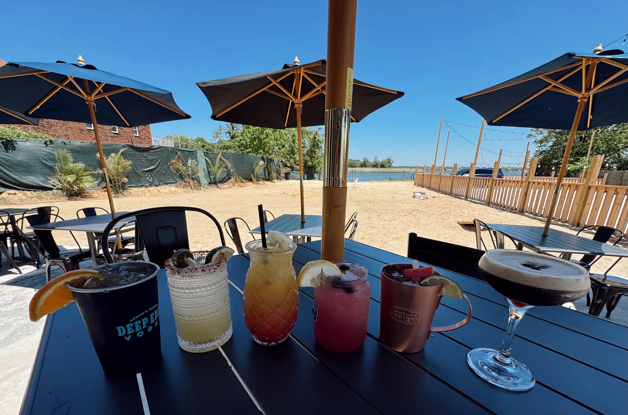 six different cocktails on a table outside overlooking the sand and water