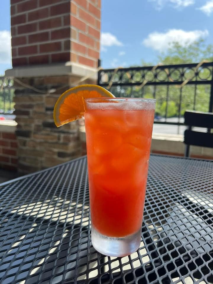 a red cocktail with an orange wedge